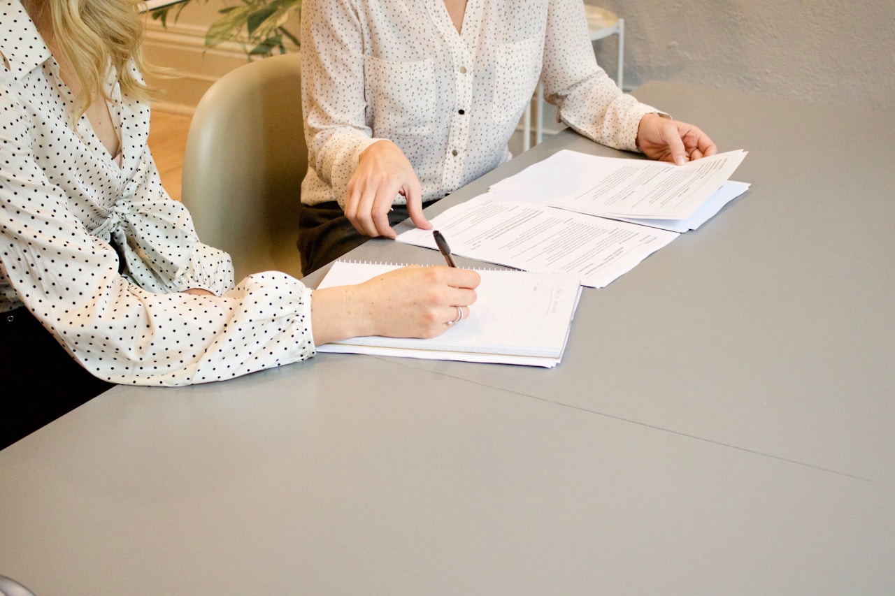 Two women sat at a desk reviewing contracts, with one signing